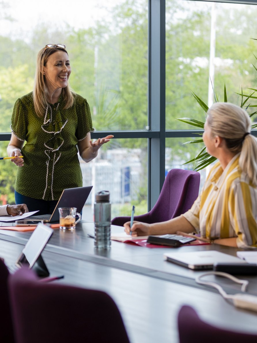 A female leader presenting to a colleague in a conference room.