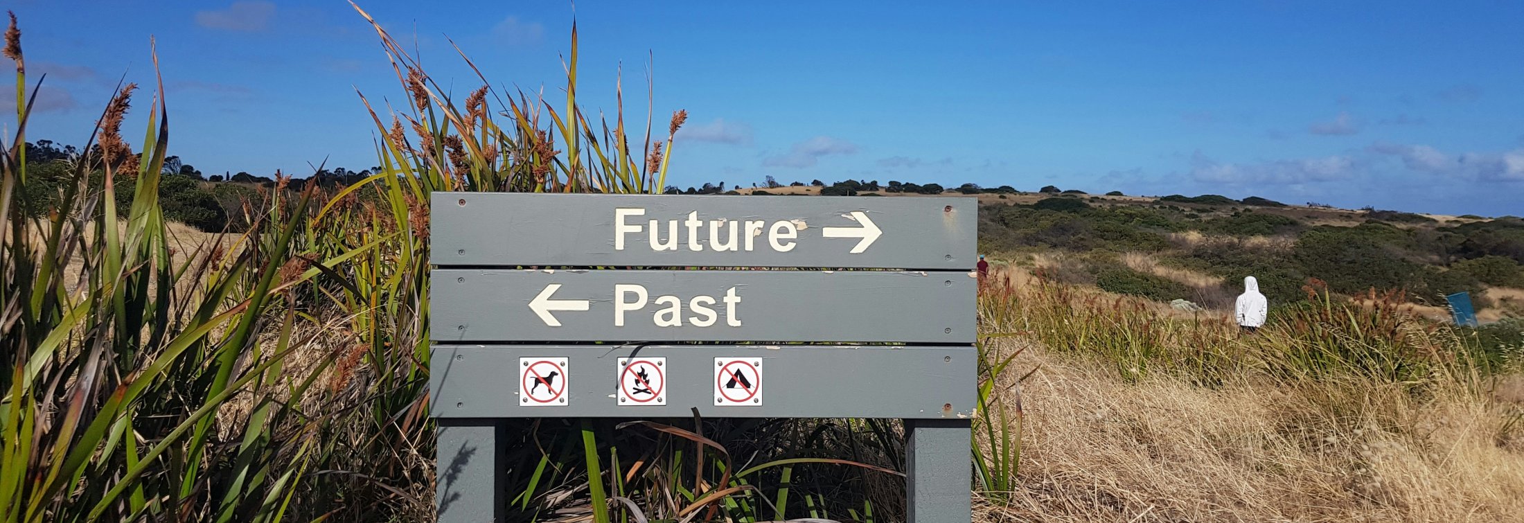 Sign on a sandy beach pointing to future and past